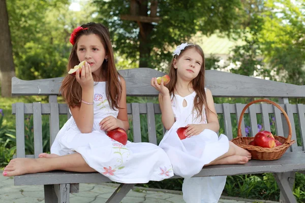 Hermosas chicas con cesta de manzanas rojas en un banco — Foto de Stock