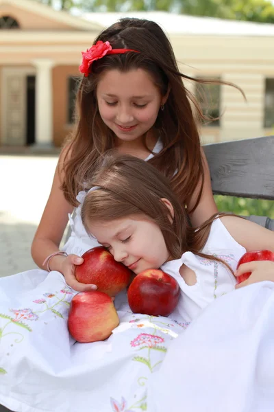 Прекрасные девушки с корзиной красных яблок на скамейке — стоковое фото