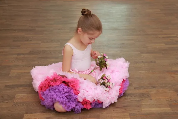 Charming child in a beautiful lush dance skirt sitting on a hardwood floor — Stock Photo, Image