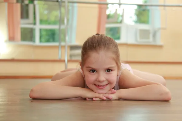 Linda joven gimnasta en un traje para el gimnasio calentándose en el suelo de madera en la sala de ballet — Foto de Stock