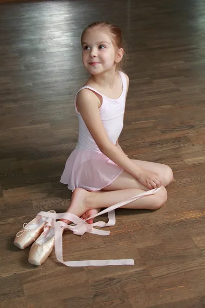 Молодая балерина надевает пуанты в балетном классе на старом деревянном танцполе — стоковое фото