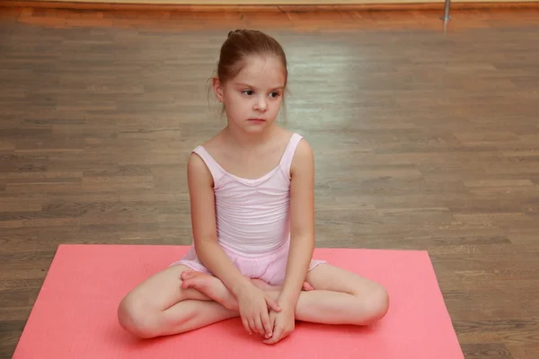 Linda joven gimnasta en un traje para el gimnasio calentándose en el suelo de madera en la sala de ballet — Foto de Stock