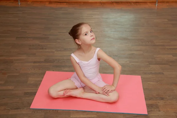 Cute young gymnast in a suit for the gym warming up on the wooden floor in the ballet hall — Stock Photo, Image