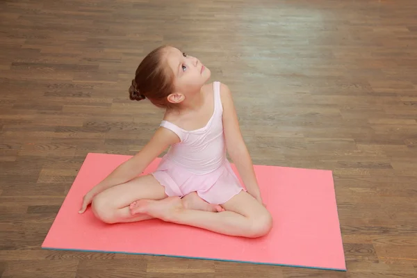 Cute young gymnast in a suit for the gym warming up on the wooden floor in the ballet hall — Stock Photo, Image