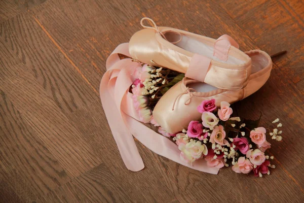 Ballet shoes with satin ribbon and a bouquet of flowers on a background of the old dark wood floor — Stock Photo, Image