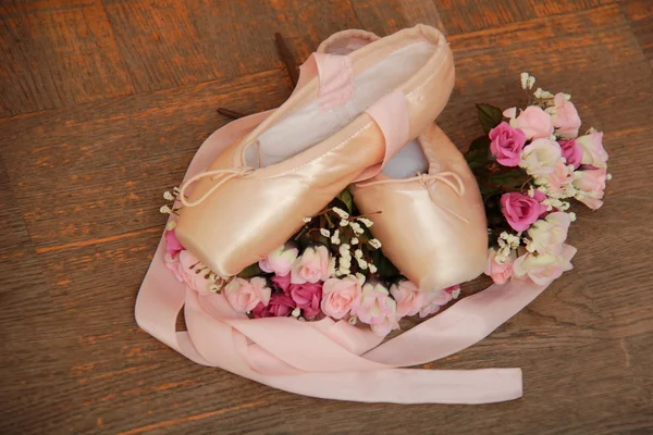 Pointe shoes with ribbons and a bouquet of flowers on a background of the old wooden floor