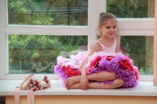 Schattig klein meisje met pointe schoenen en bloemen zittend op een vensterbank — Stockfoto