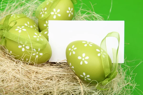 Ägg med ett mönster i påsk korg och ett oskrivet blad för hälsning text på grön bakgrund — Stockfoto