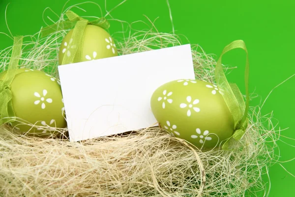Яйцо с рисунком в пасхальной корзине и чистым листом для приветствия текста на зеленом фоне — стоковое фото