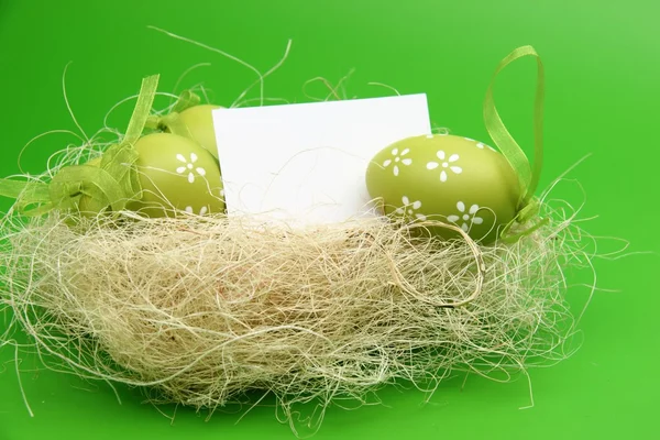 Jajko z wzorem w wielkanocnym koszyku i pusty arkusz dla tekst powitania na zielonym tle — Zdjęcie stockowe