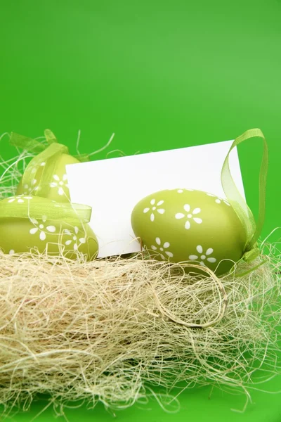 Œuf avec un motif dans le panier de Pâques et une feuille vierge pour saluer le texte sur fond vert — Photo