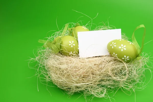 Egg with a pattern in the Easter basket and a blank sheet for greeting text on green background — Stock Photo, Image