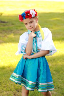 güzel bir ulusal kostüm büyüleyici bir gülümsemeyle şirin küçük kız Ukrayna yeşil çim açık havada arka plan üzerinde olduğunu.