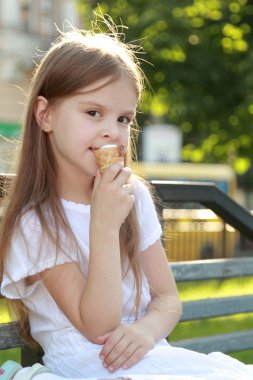 Çocuk açık havada dondurma yeme bir bankta oturur.