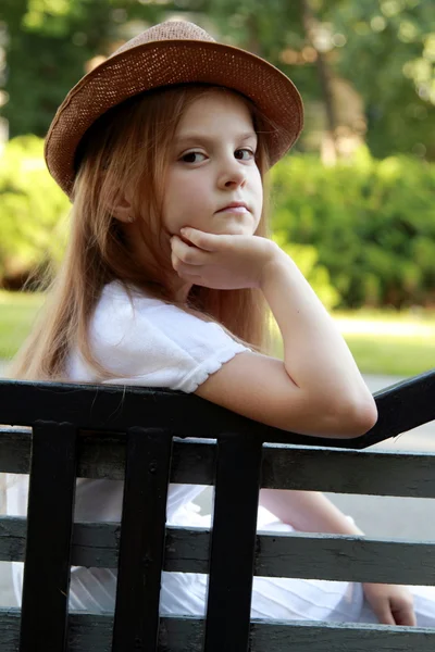 Adorabile bambina con un cappello in posa presso la fotocamera nel parco estivo all'aperto — Foto Stock