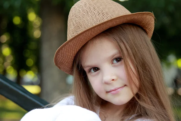 Porträtt av en liten flicka i en vit klänning i en sommar park sitter på bänken i street — Stockfoto