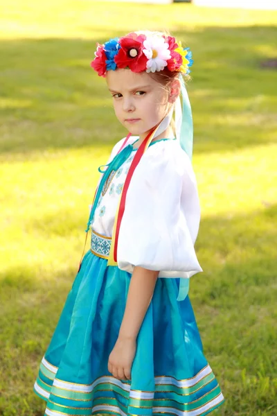 Cute little girl with a charming smile in a beautiful national costume Ukraine is on the background of green grass outdoors — Stock Photo, Image