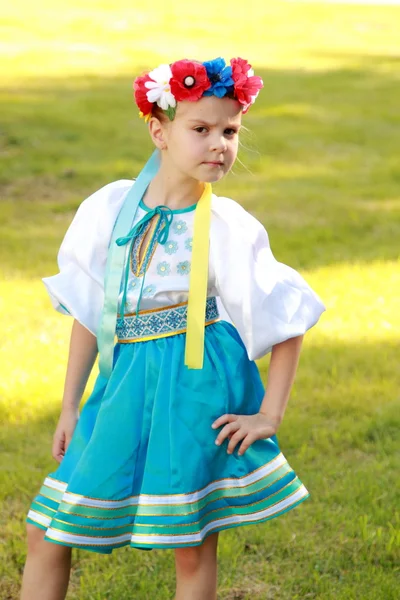 Cute little girl with a charming smile in a beautiful national costume Ukraine is on the background of green grass outdoors — Stock Photo, Image