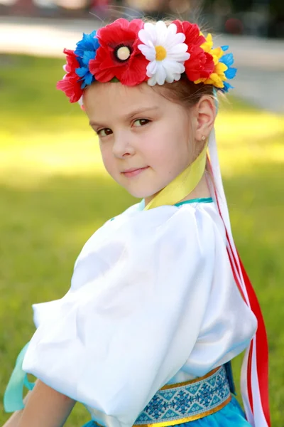 Cute little girl with a charming smile in a beautiful national costume Ukraine is on the background of green grass outdoors — Stock Photo, Image