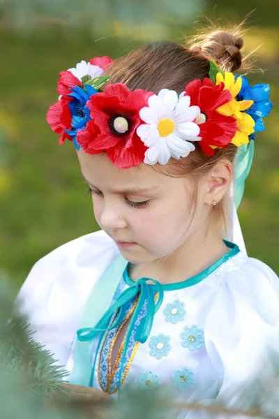 Lächelndes kleines Mädchen im hellen Nationalkostüm auf dem Hintergrund des grünen Rasens im Sommerpark — Stockfoto