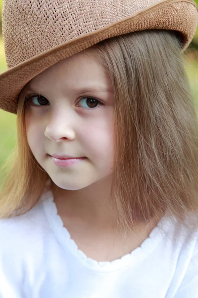 Adorable little girl with a hat posing at the camera in summer park outdoors — Stock Photo, Image