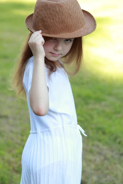 Gyönyörű kicsi lány egy fehér ruhában és kalapban a szabadban — Stock Fotó