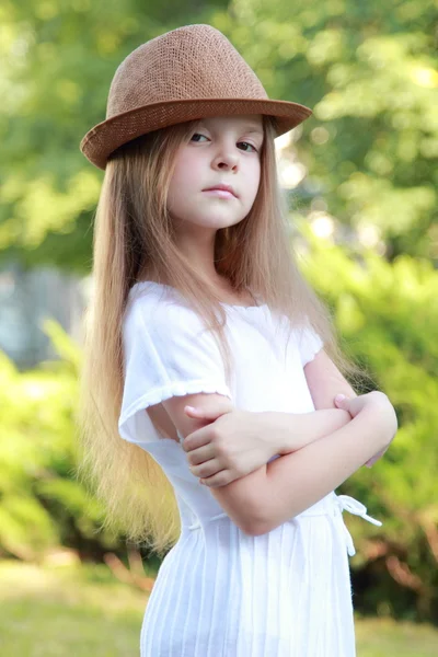 Adorable little girl with a hat posing at the camera in summer park outdoors — Stock Photo, Image