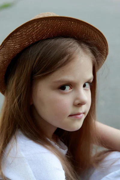Portret van een klein meisje in een witte jurk in een zomer park zit op de Bank in straat — Stockfoto