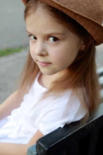 Retrato de una niña en un vestido blanco en un parque de verano se sienta en el banco en la calle — Foto de Stock