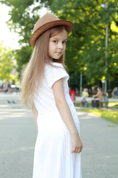 Adorable little girl with a hat posing at the camera in summer park outdoors — Stock Photo, Image