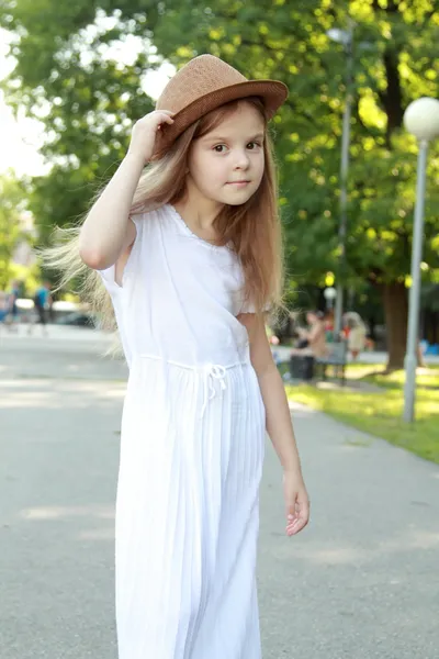 Очаровательная маленькая девочка в шляпе позирует перед камерой в летнем парке на открытом воздухе — стоковое фото