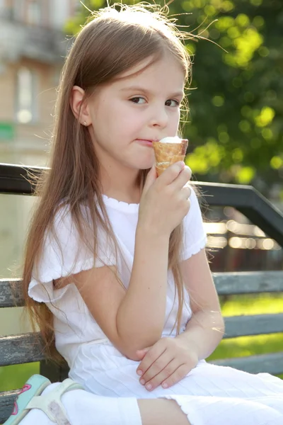 Kleines Mädchen im weißen Kleid ist weißes Eis im Freien — Stockfoto