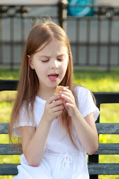 Child sits on a bench eating ice cream outdoors — Stock Photo, Image