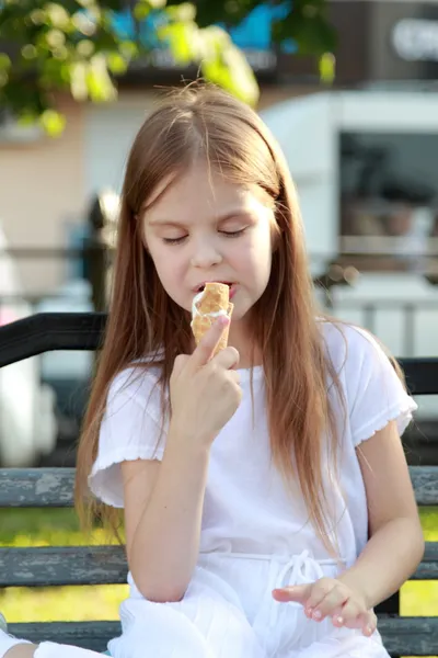 Dziecko siedzi na ławce na zewnątrz jeść lody — Zdjęcie stockowe