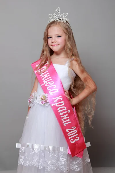 Charming little blonde in a beautiful white dress and a crown won the competition little princesses — Stock Photo, Image