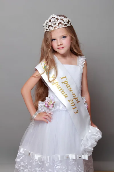 Счастливая маленькая девочка с длинными волосами в короне и белом платье с лентой и словами "Гран-при Украины 2013" на Beauty and Fashion — стоковое фото