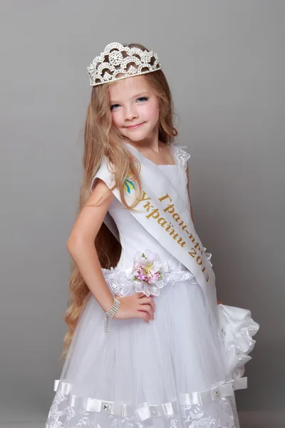 Niña feliz con el pelo largo con una corona y un vestido blanco con una cinta y las palabras "Gran Premio de Ucrania 2013" en Belleza y Moda —  Fotos de Stock