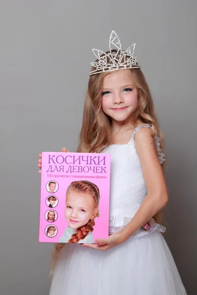 Niña caucásica con hermoso pelo largo en la corona y un vestido blanco con una linda sonrisa posando en la cámara sobre un fondo gris en la belleza y la moda —  Fotos de Stock