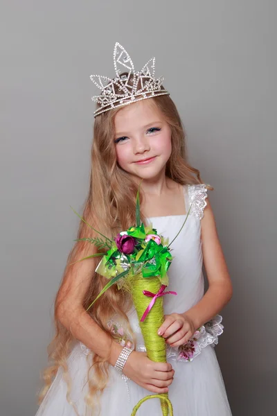 Petite fille caucasienne avec de beaux cheveux longs dans la couronne et une robe blanche avec un sourire mignon posant à la caméra sur un fond gris — Photo