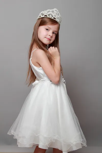 Mała dziewczynka kaukaski z piękne włosy w koronie i białą sukienkę z ładny uśmiech, pozowanie na kamery na szarym tle — Zdjęcie stockowe