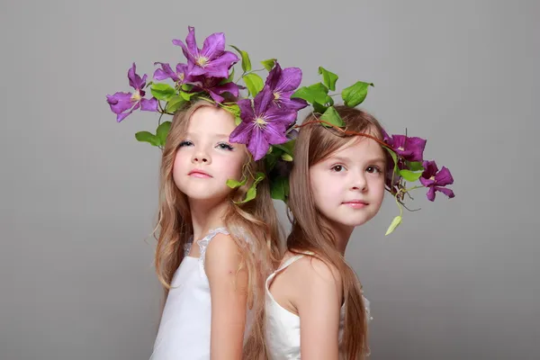 Leende liten flicka i eleganta klänningar med vackra frisyrer med färska lila klematis på skönhet och mode — Stockfoto