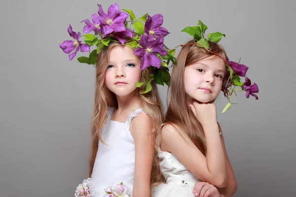 Zwei hübsche kleine Mädchen in weißen Kleidern und Frisuren aus frischen Klematis — Stockfoto