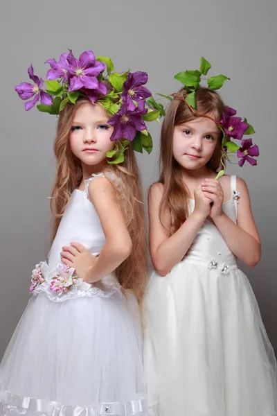 Smiling little girl in elegant dresses with beautiful hairstyles with fresh purple clematis on Beauty and Fashion — Stock Photo, Image