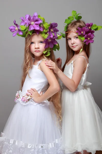 Lächelndes kleines Mädchen in eleganten Kleidern mit schönen Frisuren mit frischen lila Klematis auf Schönheit und Mode — Stockfoto