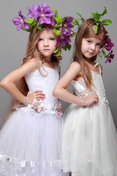 Niña sonriente en vestidos elegantes con hermosos peinados con clematis púrpura fresca en la belleza y la moda —  Fotos de Stock