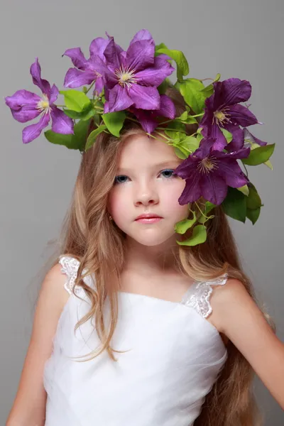 Caucasian cute little girl with beautiful hairstyle with fresh bright clematis smiles and poses for the camera — Stock Photo, Image