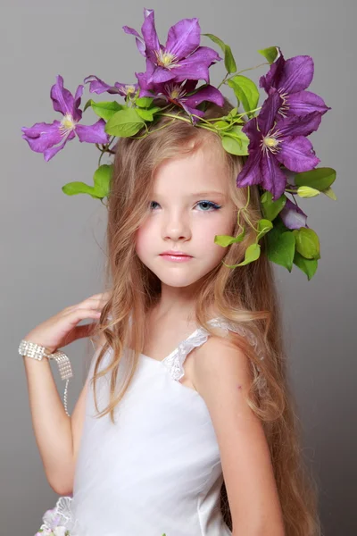 Glücklich niedliches kleines Mädchen mit entzückender Frisur der lila Klematis lächelt in die Kamera auf grauem Hintergrund — Stockfoto