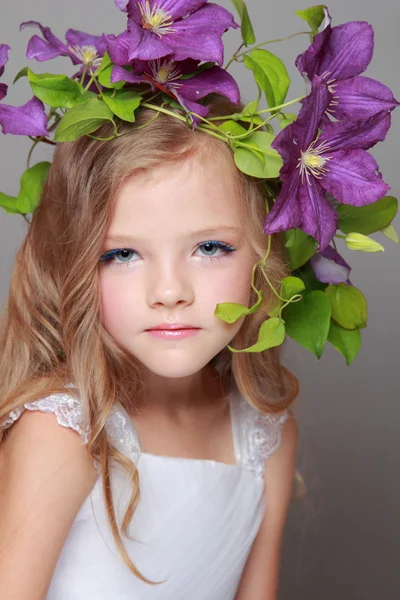 Caucasian cute little girl with beautiful hairstyle with fresh bright clematis smiles and poses for the camera — Stock Photo, Image