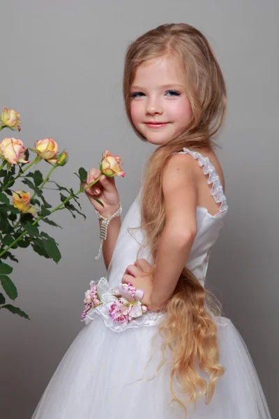 Caucasian girl with beautiful healthy long hairs holding yellow roses with green leaves on a gray background — Stock Photo, Image