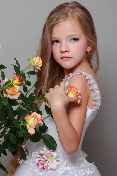 Studio bild av en vacker liten flicka med långa blonda hår nära de färska rosorna på skönhet och mode — Stockfoto